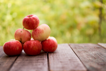 Red apples lie on a wooden board. Green blurred background. Close-up.