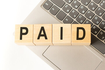 Word paid. Wooden cubes with letters isolated on a laptop keyboard. Business Concept image.