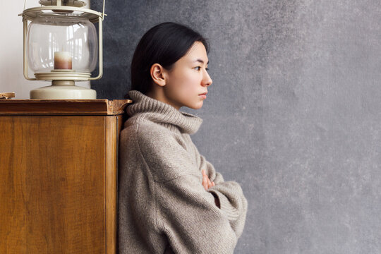 Winter style portrait of brunette asian woman posing indoor in big cozy warm sweater