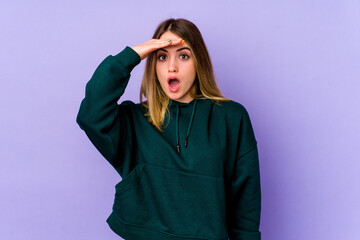 Young caucasian woman isolated on purple background looking far away keeping hand on forehead.