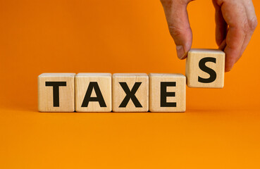 Wooden cubes with word 'taxes'. Male hand. Beautiful orange background. Business concept. Copy...