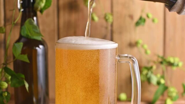 Beer. Cold Craft light Beer in a glass with water drops. Pint of Beer close up on a wooden background. Beer is pouring from the bottle. Border design. High quality 4k footage
