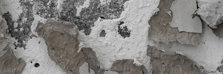 Peeling paint on the wall. Panorama of a concrete wall with old cracked flaking paint. Weathered rough painted surface with patterns of cracks and peeling. Wide panoramic texture for grunge background