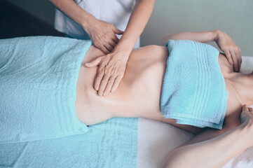 Young unrecognizable woman lying on massage table and enjoying therapeutic massage. Body care,...