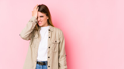 Young caucasian woman isolated on pink background forgetting something, slapping forehead with palm and closing eyes.