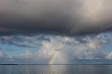 Naklejka na ściany i meble A beautiful rainbow appears over the calm sea in Raja Ampat, Indonesia. This remote, tropical region is known for its incredible marine biodiversity.