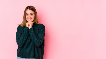 Young caucasian woman isolated on pink background keeps hands under chin, is looking happily aside.