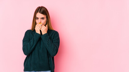 Young caucasian woman isolated on pink background covering mouth with hands looking worried.