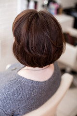 Female back with short, straight, brunette hair in hairdressing salon