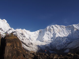 A mountain climber standing in front of a snow-covered Himalayas in the blue skies, ABC (Annapurna...