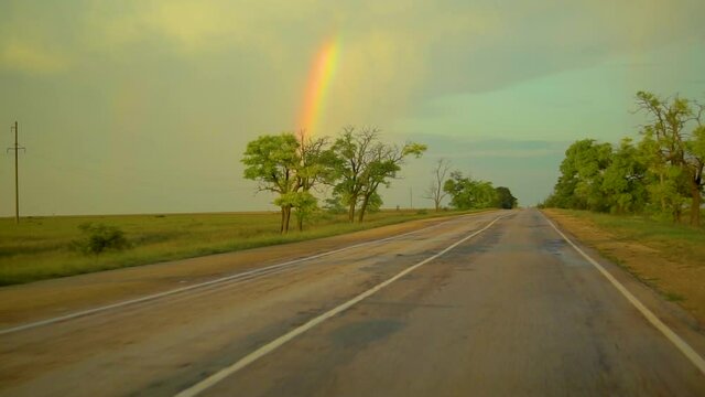 Rainbow on the road, rides a car on the highway and see a large romantic multicolored bridge, around the trees