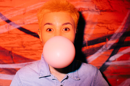 Happy young asian woman with short yellow hairs doing bubble gum