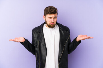 Young man isolated on purple background doubting and shrugging shoulders in questioning gesture.