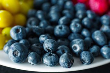 View from above. A mix of yellow, red and blue berries in a white grater. Triangle separation. Summer mix of fruits. Berry layout