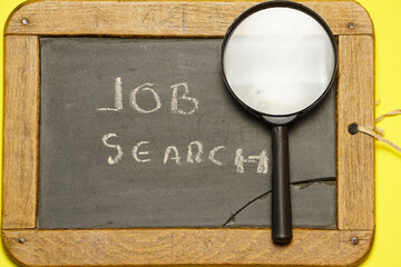 Top view of magnifying glass on blackboard with job search message. flat lay