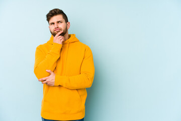 Young caucasian man isolated on blue background thinking and looking up, being reflective, contemplating, having a fantasy.