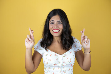 Beautiful woman over yellow background gesturing finger crossed smiling with hope and looking side