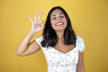 Beautiful woman over yellow background doing ok sign with fingers and smiling, excellent symbol
