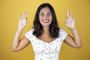 Beautiful woman over yellow background doing ok sign with fingers and smiling, excellent symbol