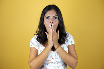 Beautiful woman over yellow background surprised putting her hands on her mouth