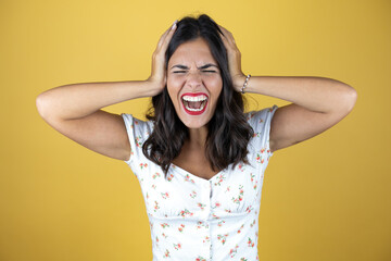Fototapeta premium Beautiful woman over yellow background suffering from headache desperate and stressed because pain and migraine with her hands on head