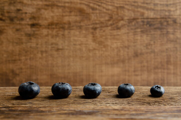 five blueberries of different size on wooden background