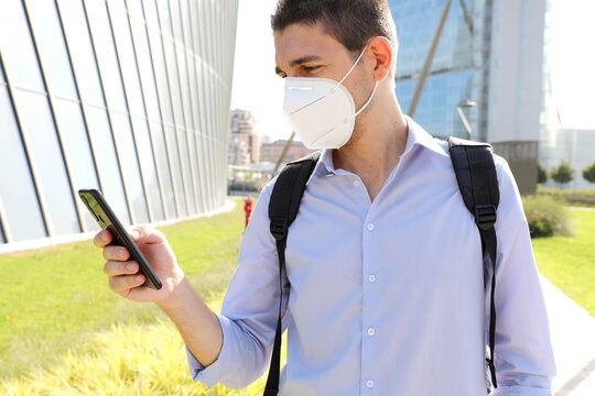 COVID-19 Young Business Man Wearing KN95 Protective Mask Using Smartphone App In Modern City Street