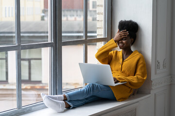 Happy African American woman freelancer with afro hairstyle wear yellow cardigan sitting on...