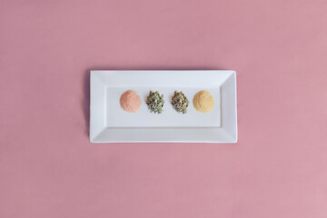 An elegant white plate set in the middle of a table with a pastel pink tablecloth contains dried leaves and powdered spices for cooking. Healthy food.