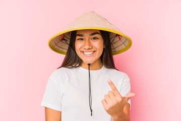 Young asian woman wearing a vietnamese hat isolated Young asian woman wearing a vietnamin hatpointing with finger at you as if inviting come closer.