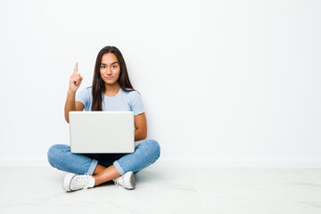 Young mixed race indian woman sitting working on laptop showing number one with finger.