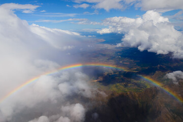 Aerial view of rainbow in front of clouds. Sun light and rainy clouds forming a beautiful atmospheric weather. Cloudscape from above.