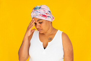 indigenous woman wearing head wrap with hand to forehead against yellow background