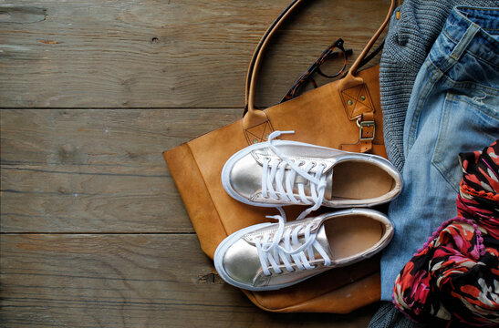 Tan leather tote bag with various travel items on wooden floorboards