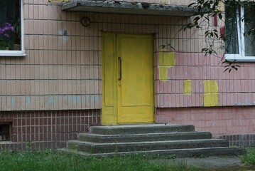 old closed wooden yellow door on brown wall with concrete gray threshold outside