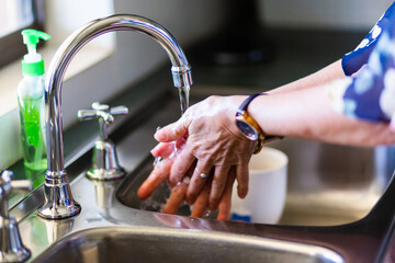 senior woman washing hands with soap in the kitchen sink