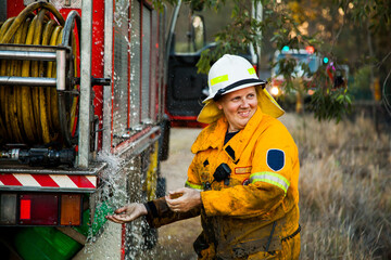 Firefighter laughing and washing her hands besides fire truck