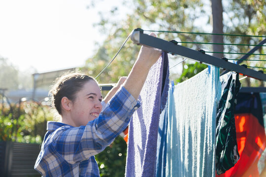Young woman pegging clothes to washing line in backyard