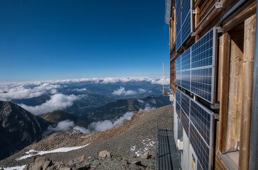 Solar panels mounted on the mountain refuge hut walls providing necessary electricity for a guest' needs with wide-angle Alps mountains landscape view.