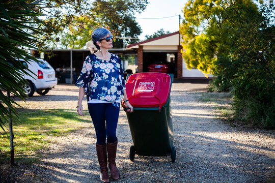 Middle aged woman taking rubbish bin out for collection