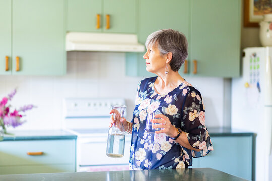 Middle aged woman pouring a glass of water in her kitchen