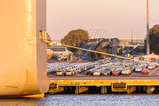 Rows of cars sit on the docks next to a cargo ship at the Port of Brisbane