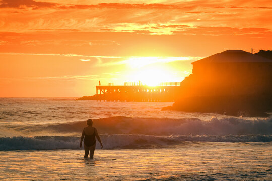 A woman at the beach at sunrise, wharf in the background.