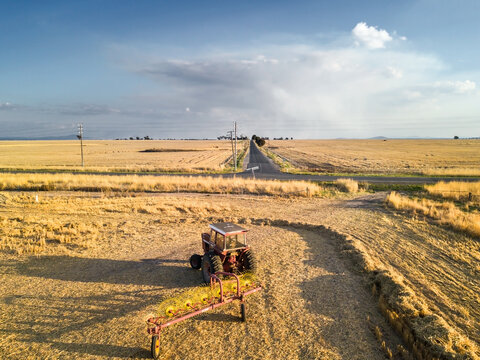 Looking down on a tractor and raking equipment sitting on farmland with smoke clouds on the horizon.