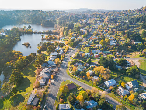 An aerial view of a road lined with Autumn trees and lakes running through a country town