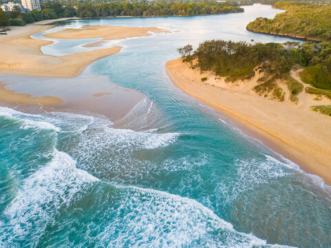 Aerial view of a river winding out to sea over a sandy beach