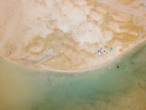 Aerial view of beachgoers on a sand bank of a tidal estuary