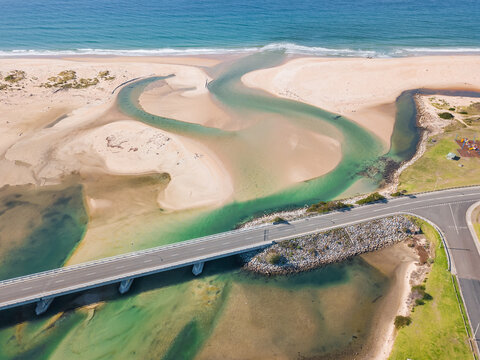 Aerial view of a river flowing under a road bridges and winding out to sea.