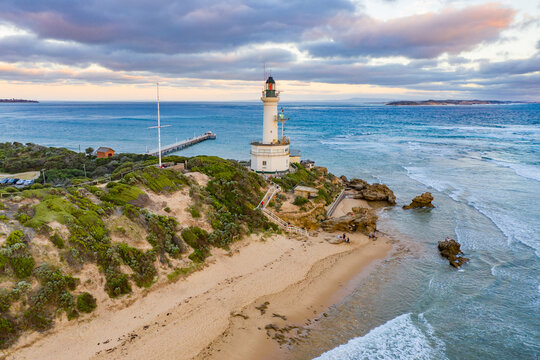 Aerial view of a lighthouse sitting on a rocky point at the entrance to a large bay