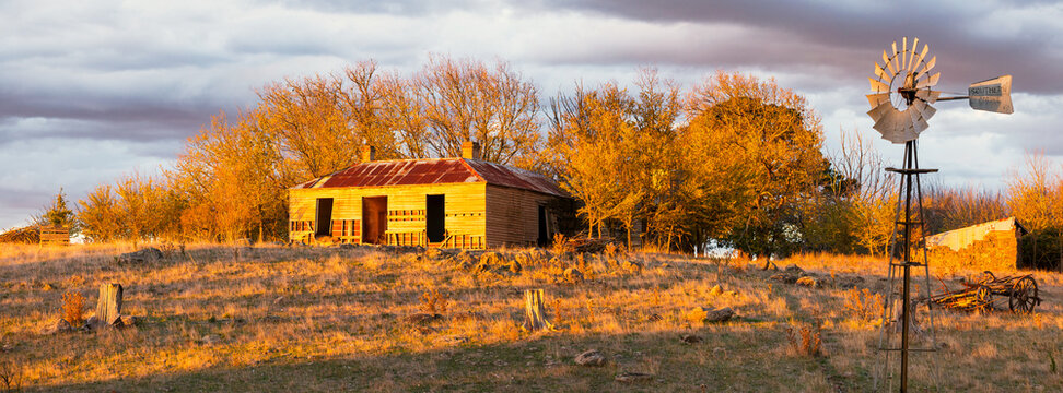 Ruins of an old farmhouse and windmill surrounded by autumn trees in a dry paddock